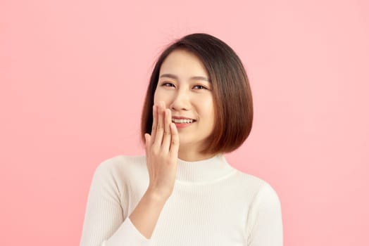 Beautiful Asian woman showing hand while smiling. Over pink background