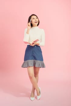 Full length portrait of a smiling beautiful woman holding isolated on a pink background. 