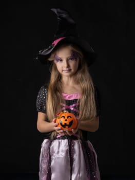 Cute halloween witch girl in fantasy costume holding pumpkin bucket with candy worms, isolated on black background