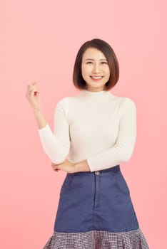 Cheerful young beautiful Asian woman showing her hand while standing over pink background.