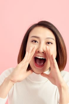 Young woman is holding hands near mouth and telling a secret on a pink background