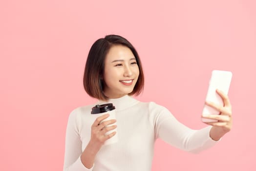 Young Asian woman selfie with her coffee cup on pink background.