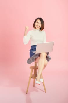 Young Asian woman using credit card to payment online with her laptop. Isolated on pink background.