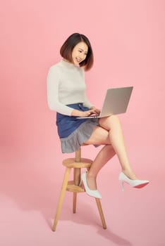 Young Asian woman using laptop while sitting on chair.