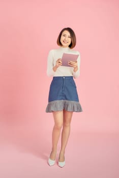 Beautiful Asian woman hodling book and reading over pink background. Full length.