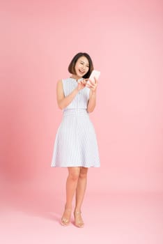 Full length portrait of a smiling casual girl using mobile phone isolated over pink background