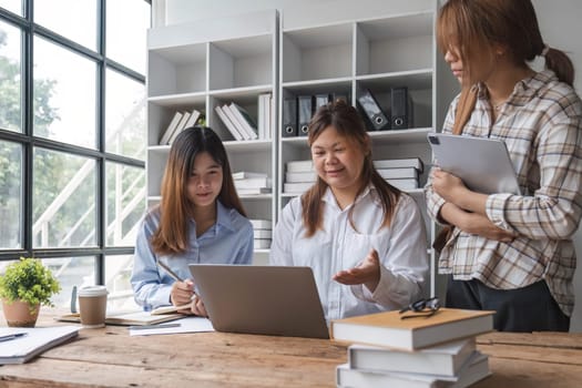 Asian College groups of students using laptop, tablet, studying together with notebooks documents paper for report near windows in classroom. Happy young study for school assignment