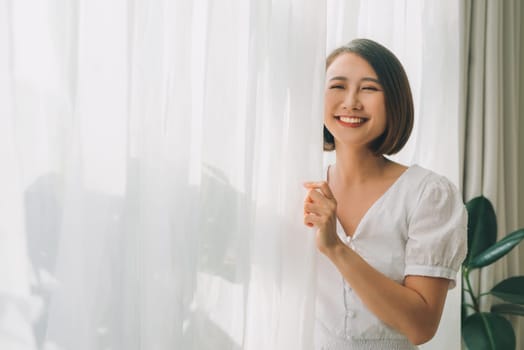 Side view of a happy woman opening curtains of a window and enjoying a new day with a warm light from outdoors