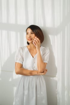 Young Asian woman talking on smartphone against white wall