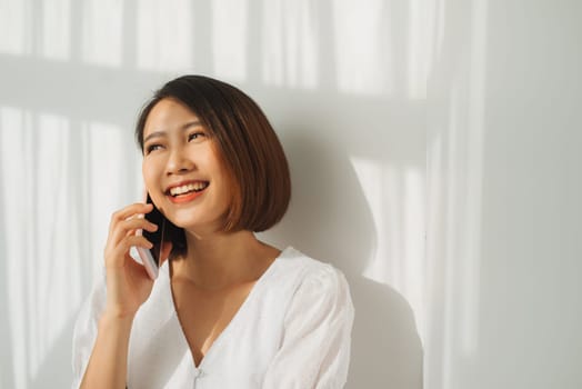 Asian young woman over isolated white wall keeping a conversation with the mobile phone