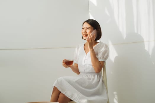 Asian young woman over isolated white wall keeping a conversation with the mobile phone