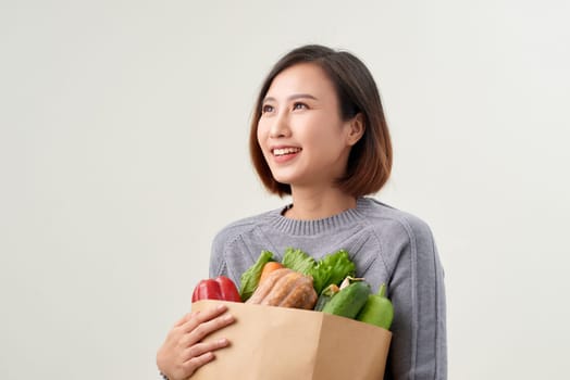 Cheerful woman holding a shopping bag full of groceries