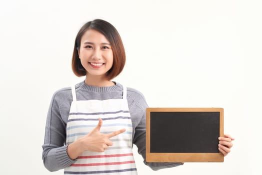 Asian waitress pointing at empty board and looking at camera while standing on white background