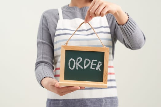 Cheerful girl holding advertising board with order word and pointing on it, white studio background