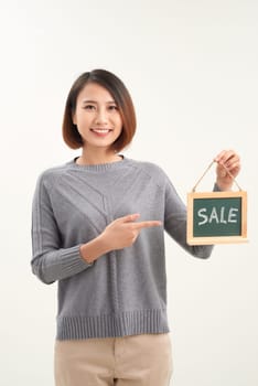 Cheerful girl holding  advertising board with sale word and pointing on it, white studio background