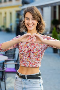 I love you. Caucasian woman makes symbol of love showing heart sign to camera express romantic feelings express sincere positive feelings. Charity gratitude donation. Outdoors in city street. Vertical