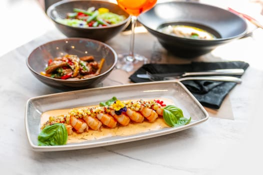 Fried shrimp in creamy sauce with mango and basil on a gray plate in a restaurant. High quality photo