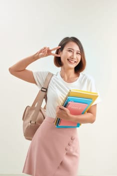 Cheerful pupil being in good mood after passing exam, shows with gesture everything is excellent, holds colourful folders  isolated over white background