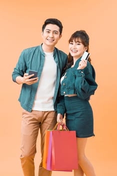 Young couple with credit cards, shopping bags and mobile phone on color background