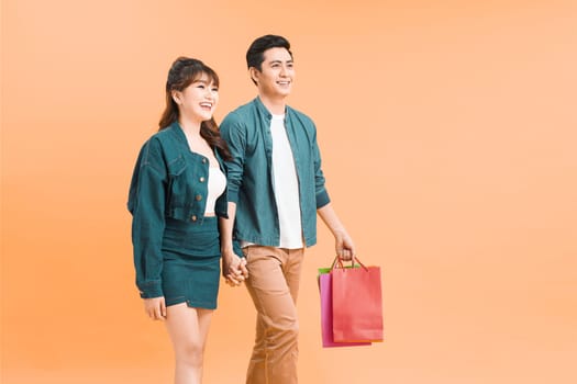 Happy asian couple holding shopping bags and smiling at camera isolated