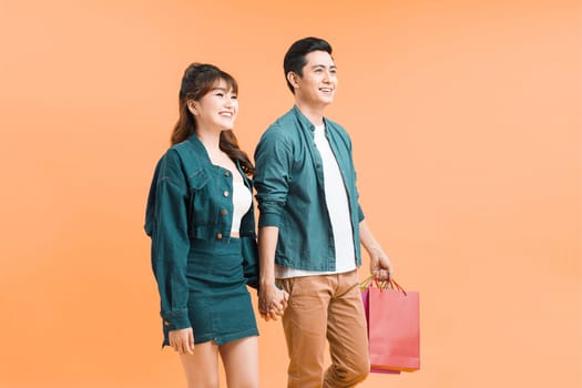 young couple walking with shopping bags isolated on color background