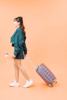 Travel concept. Full length studio portrait of pretty young woman holding passport with tickets walking with luggage