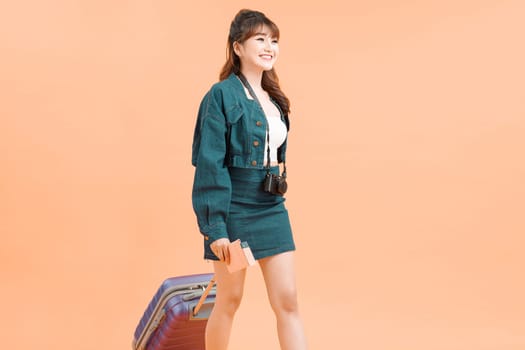 A cheerful young asian woman dressed holding passport with flying tickets while standing with a suitcase 