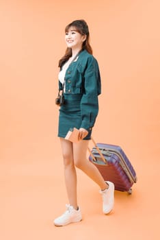 Travel concept. Full length studio portrait of pretty young woman holding passport with tickets walking with luggage
