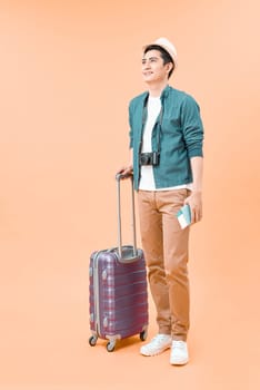 Happy asian male traveler walking with suitcase against isolated color background