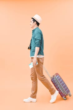 Happy asian male traveler walking with suitcase against color background