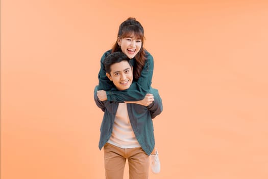 Handsome man giving piggy back to his girlfriend on color background