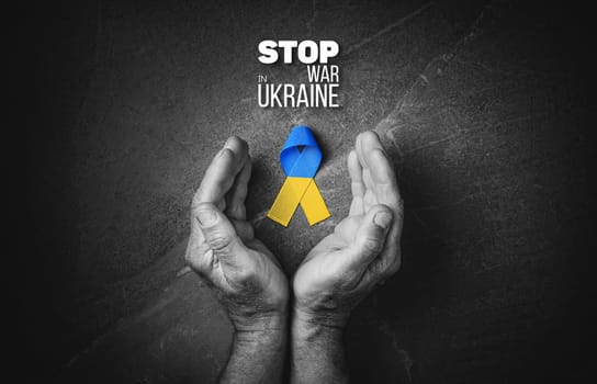 male hand with yellow and blue ribbon on marble background with words stop war in ukraine black and white color. concept needs help and support, truth will win