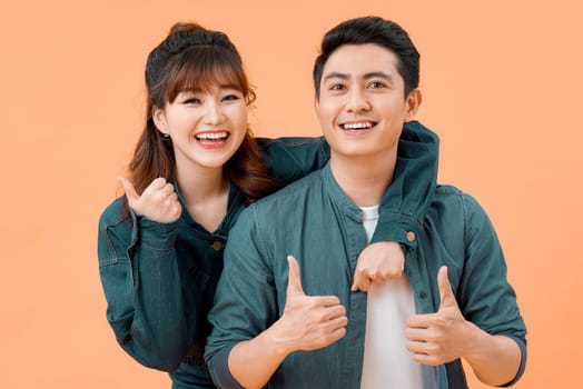 Portrait of a cheerful young couple standing together isolated over yellow background, showing thumbs up