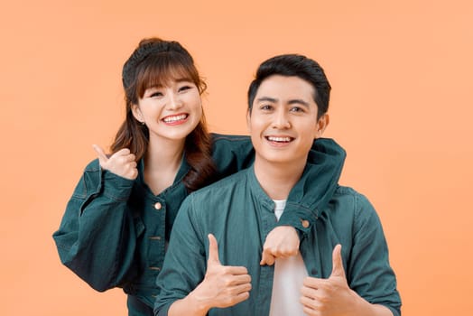 Happy young couple showing thumbs up and looking at camera isolated over yellow background