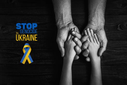 male hands hold childrens on a dark background with words stop genocide in ukraine with yellow and blue ribbon. black and white color. concept needs help and support, truth will win