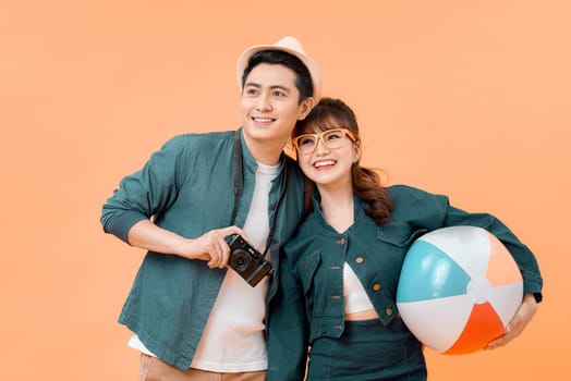 Young attractive couple with beach ball and camera on yellow background