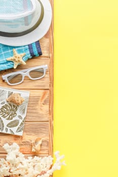 Beach hat with shorts and sunglasses on wooden background with yellow copy space. Flat lay. Summer vacation concept. Corals and seashell. Top view.
