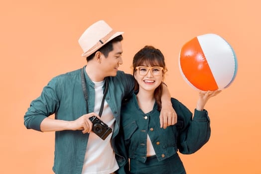 Young attractive couple with inflatable ball and camera on yellow background