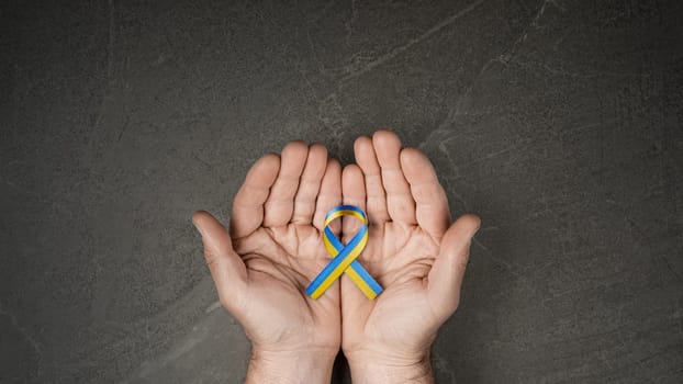 male hand with yellow and blue ribbon on marble background. concept needs help and support, truth will win