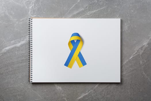 ukrainian yellow blue ribbon in the middle of notebook on marble table. concept needs help and support, truth will win