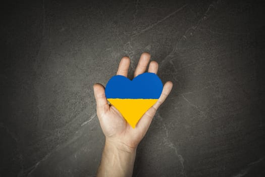 male hand hold painted yellow and blue heart on grey marble background. concept needs help and support, truth will win