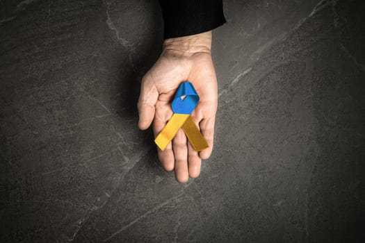 old man hand with yellow and blue ribbon on marble background. concept needs help and support, truth will win