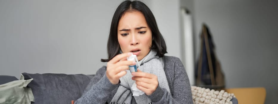 Ill korean woman looking at thermometer with concerned face, catching cold, having fever, having covid, staying at home on sick leave.