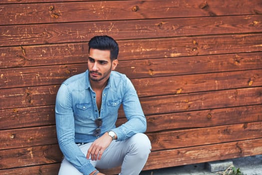 A man sitting on the ground in front of a wooden wall