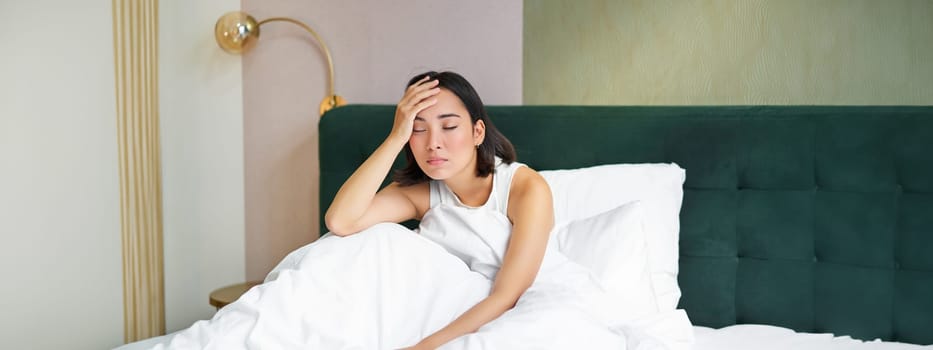 Portrait of sad young woman waking up, feeling bad, wants to sleep, wakes early morning, looking lazy and upset.