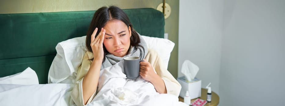 Flu, sickness and people. Young woman feeling sick, having fever and catching col, lying in bed with hot tea, taking drugs from influenza.