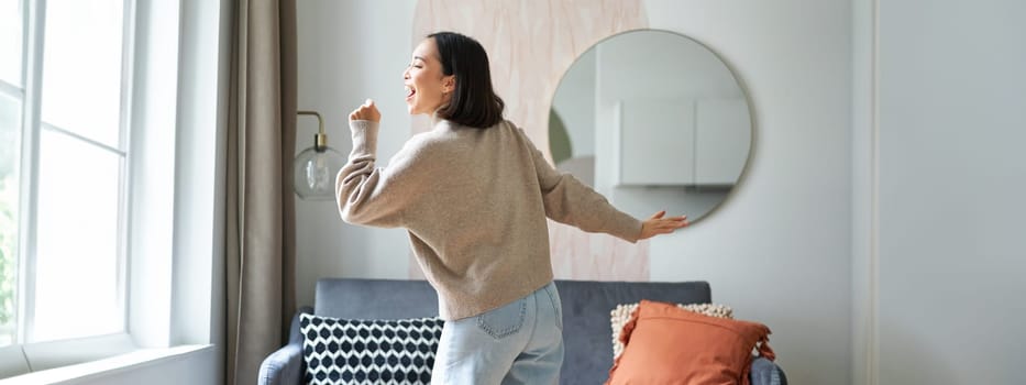 Beautiful asian woman dancing, feeling happy and upbeat, singing into hand microphone, express joy, positivity and happiness.