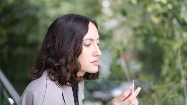 A young woman with beautiful curly hair is thoughtfully smoking a cigarette while enjoying a serene outdoor setting