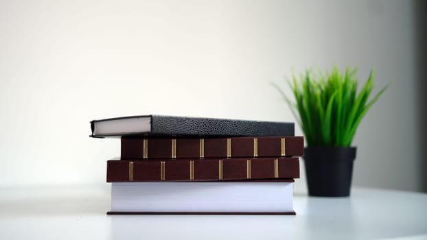Enjoy a neat stack of books beside a vibrant green plant, perfect for enhancing your study area or home decor
