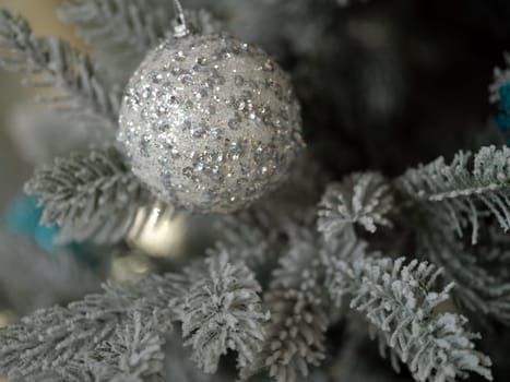 An exquisite silver ornament, beautifully adorned with glitter, hangs delicately on a frosted Christmas tree